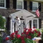 "Professional exterior house painter in Philadelphia painting the trim of a stone home with black shutters and American flag."