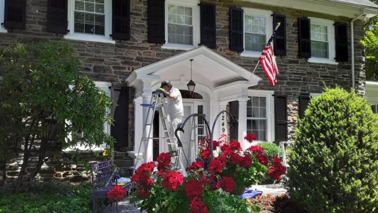 "Professional exterior house painter in Philadelphia painting the trim of a stone home with black shutters and American flag."