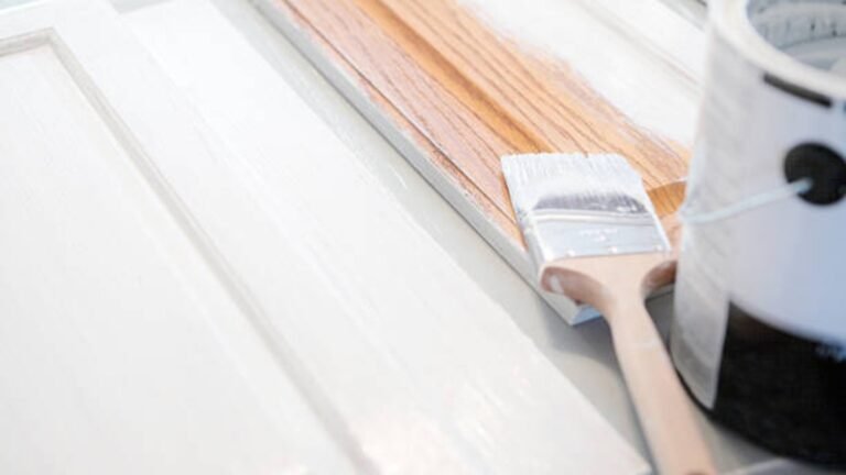 Paintbrush applying white paint on kitchen cabinet surface in Philadelphia.